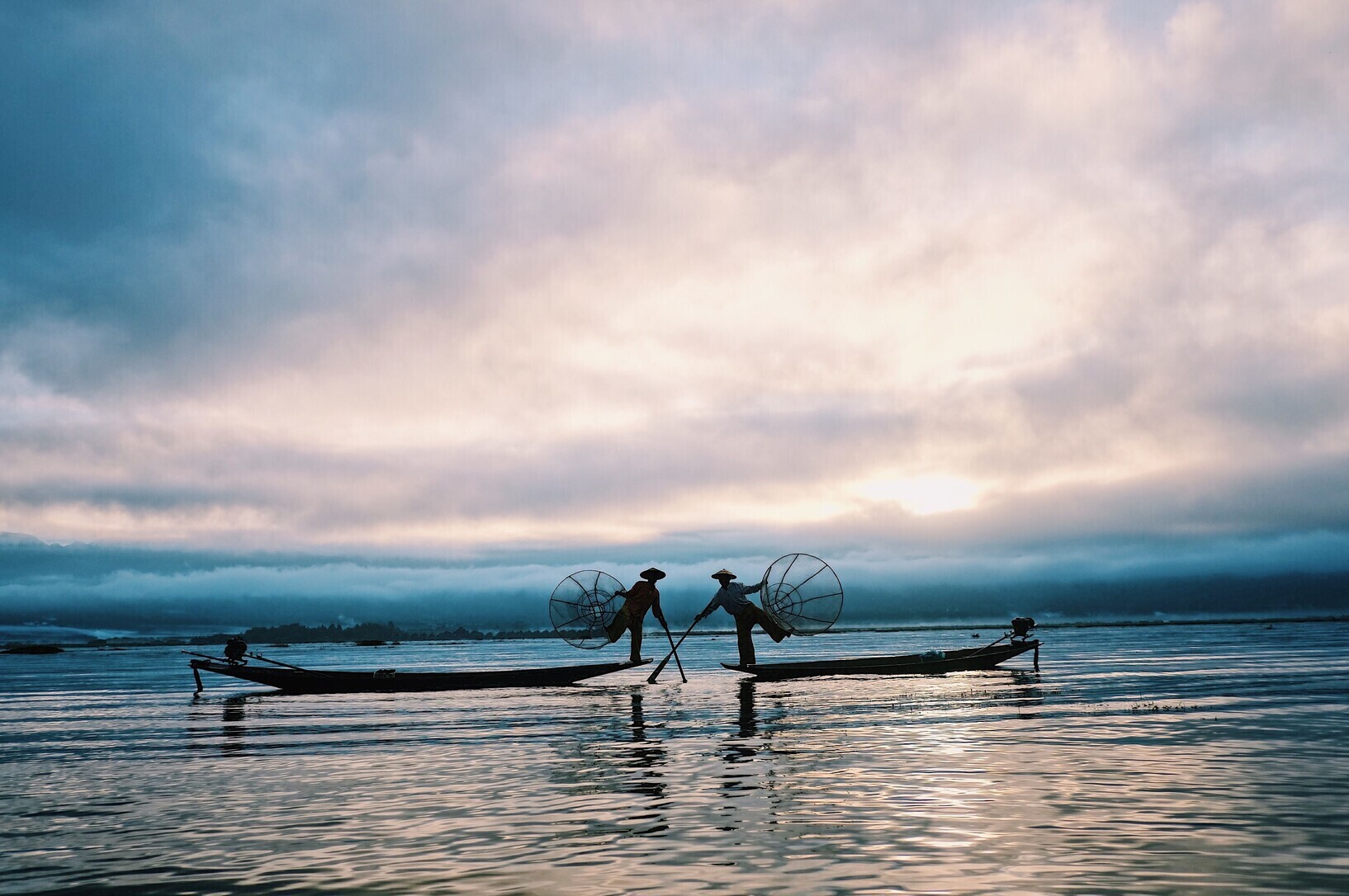 Silhouettes of fishermen fishing with traditional nets at sunrise on Inle Lake, Myanmar.